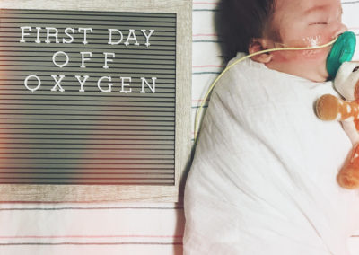 Infant next to a sign that says, "first day off oxygen."